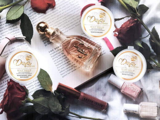 Flat lay: Daya's Essence wax melts, perfume, book, beauty products, symbolizing luxury fragrance.