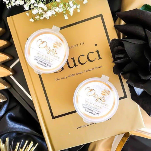 Two "Raspberry and Rhubarb" wax melts on Gucci book, hinting at luxurious fragrance experience.