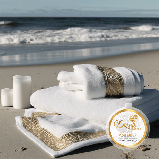 A 1oz tub with a branded sticker displaying the scent name "Beach Towels " Dayas Essence, 30% concentrated wax melt. The tub is positioned at the bottom right, against a backdrop of White towels, adorned with a gold detailed pattern along the edges, which are neatly arranged on a sandy beach, creating a serene and inviting atmosphere. Two white candles stand adjacent to the towels, In the background, the shimmering blue sea stretches out, inviting you to bask in the tranquility of a beach getaway.